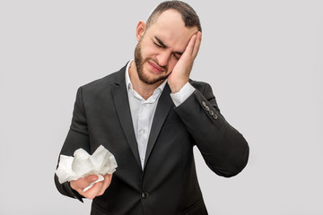 Sick young man in suit stand and lean head on hand. There is white tissue in another one. He suffer...