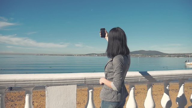 Back view of a woman taking photograph with a smart phone camera at the horizon on the beach.Young girl taking photos of blue sea on mobile phone.