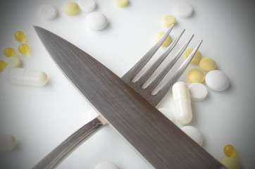 Pills in a white plate with fork and knife. The concept of imposing drugs.