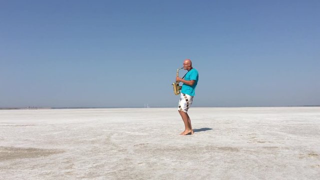 Saxophonist plays and stands on the board for a kite against the background of white salt lake 2