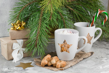 Obraz na płótnie Canvas gift boxes,mug with drink decorated with marshmallow and star shape cookies near evergreen christmas tree branches gray concrete background