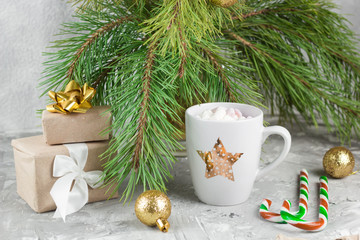 gift boxes, hot drink with marshmallows, candy canes and golden balls on shabby gray background with evergreen christmas tree branches