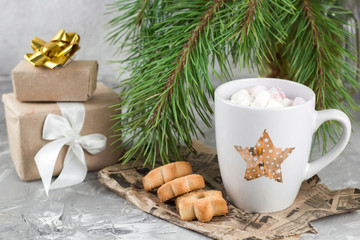 Obraz na płótnie Canvas gift boxes,mug with drink decorated with marshmallow and star shape cookies near evergreen christmas tree branches gray concrete background