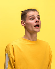 The surprised and astonished young man screaming with open mouth isolated on yellow background. concept of shock face emotion