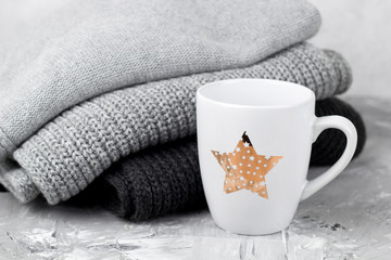 cute white cup with drink and gray knitted sweaters and scarf, cozy autumn  or winter weekends concept