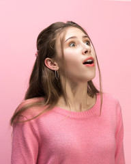The surprised and astonished young woman screaming with open mouth isolated on pink background....