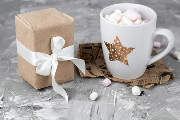 Fototapeta na wymiar cute stylish cup with marshmallows and gift box concrete gray background