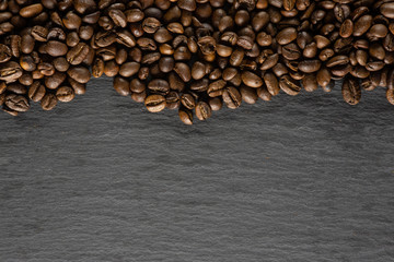 Lot of whole dark brown coffee beans sweet arabica variety above flatlay on grey stone