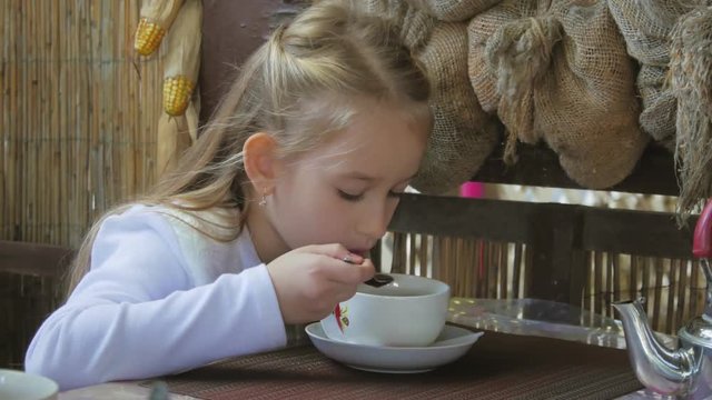 Cute little girl drinking tea in cafe. light breakfast. Little caucasian girl taking a sip of tea at the cafe.