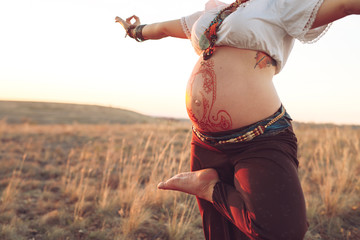 Pregnant woman doing yoga in the field at sunset.