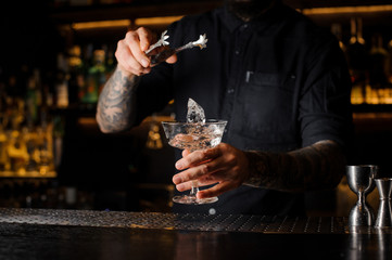 Barman putting an ice cube into a cocktail glass