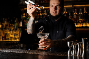 Barman with beard putting an ice cube into a cocktail glass