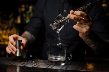 Tattooed bartender putting an ice cube into a cocktail glass