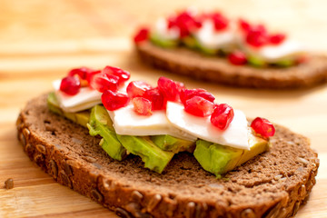Slice of bread with avocado, cherry tomato, pomegranate seeds and fresh cheese.