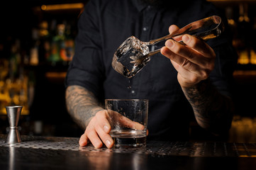 Tattooed mixologist putting an ice cube into a cocktail glass