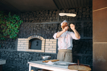 Skilled chef preparing dough for pizza rolling with hands and throwing up.