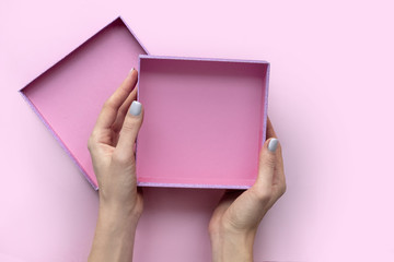 Female hands with open empty box on pink background.