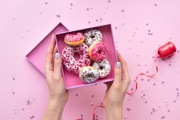 Woman hands holding  open box with colorful donuts on pink background.
