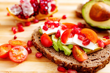 Slice of bread with avocado, cherry tomato, pomegranate seeds and fresh cheese.