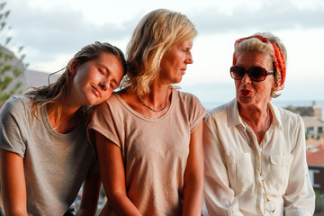 Three generations of attractive women of a family together on summer terrace. Authentic, unadorned,...