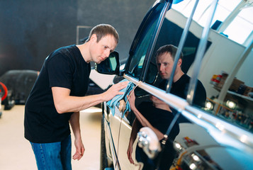 The man is wiping with a cloth body of a brilliant car.