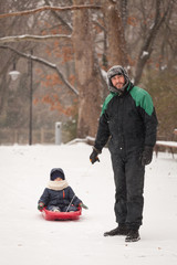 Fototapeta na wymiar Father pulls a child on a sled. Father and son sledding at winter time.