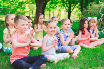 Naklejka na ściany i meble A large group of children engaged in yoga in the Park sitting on the grass.