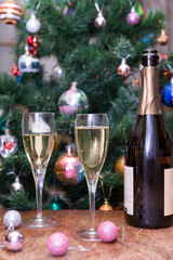 glasses of sparkling wine, a bottle of champagne, pink Christmas balls on the background of Christmas spruce