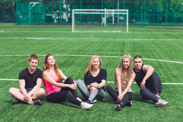Young people sit on the grass on the football field.