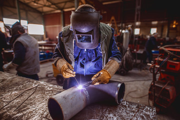 Worker welding iron. Protective suit and mask on. Workshop interior.