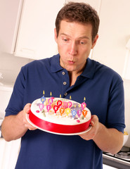 MAN BLOWING OUT CANDLES ON  BIRTHDAY CAKE