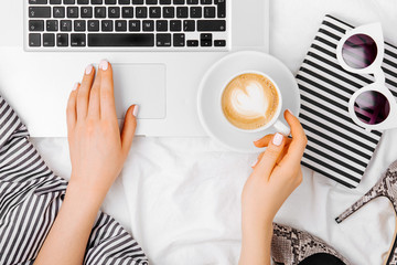 Young woman drinking coffee at home in her bed and working her laptop, top view