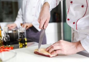 Chef cutting meat on chopping board, professional cook holding knife and cutting meat in restaurant