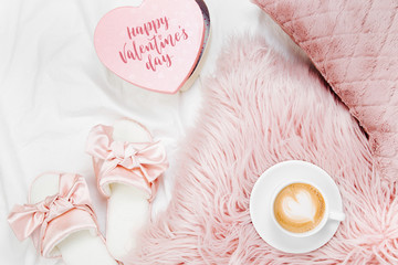 Morning concept. A cup of coffee on a pink pillow, slippers on the bed. Flat lay, top view