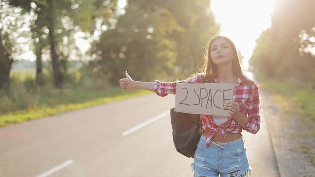 Young beautiful woman hitchhiking standing on the road holding 2 space sign. Summer time