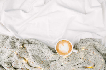 Cup of coffee on bed with warm plaid. Copy space. Flat lay, top view
