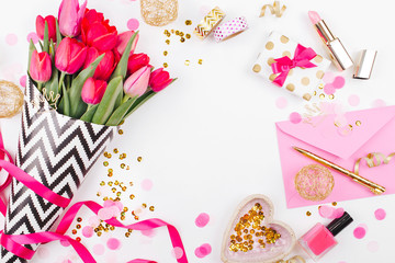 Obraz na płótnie Canvas Pink and Gold Styled Desk with Florals. Pink tulips in black and white stylish wrapping paper, gifts, cosmetics and female accessories with confetti on white background