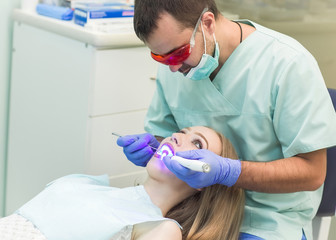 Dentist doing procedure with dental curing UV light in clinic