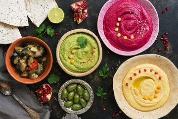 Colorful varied hummus, caponata, olives, pita and pomegranate on a dark rustic background. Vegetarian diet food.Top view, flat lay. Mediterranean food.