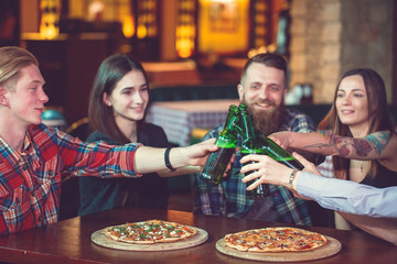 Friends having a drinks in a bar, They are sitting at a wooden table with beers and pizza.