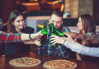 Friends having a drinks in a bar, They are sitting at a wooden table with beers and pizza.
