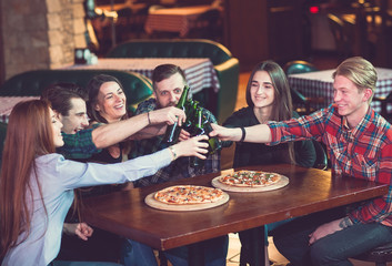 Friends having a drinks in a bar, They are sitting at a wooden table with beers and pizza.