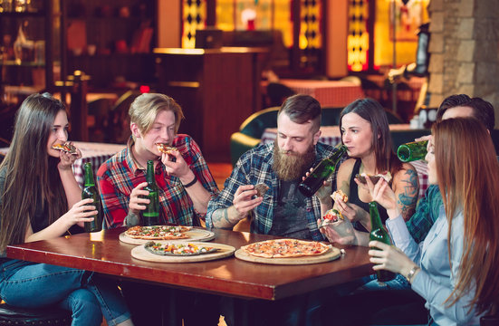 Friends having a drinks in a bar, They are sitting at a wooden table with beers and pizza.