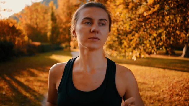 Running woman. Runner is jogging in sunny day light in the autumn trees background. Female fitness training outdoors in park, 4K
