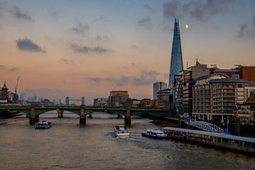 Sunset over the river Thames, London. The Shard building can be seen, with the moon to the side of it, high in the sky. 