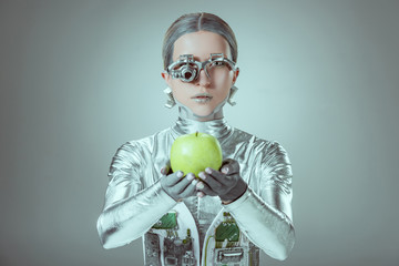 robot holding apple and looking at camera isolated on grey, future technology concept