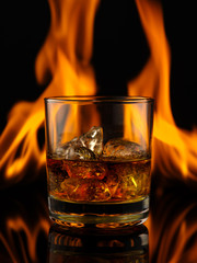 Glass of whiskey with ice on a background of fire.