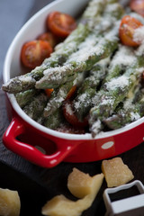 Close-up of a baking dish with asparagus, grated parmesan cheese and tomatoes, selective focus