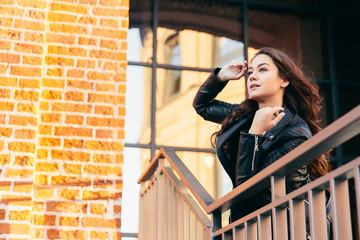 Young woman in black looking into the distance. Girl holding hand on brown bricks wall background