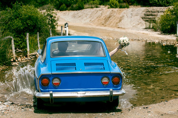 Obraz na płótnie Canvas macchina d'epoca blu sta per attraversare un guado con degli sposi dentro